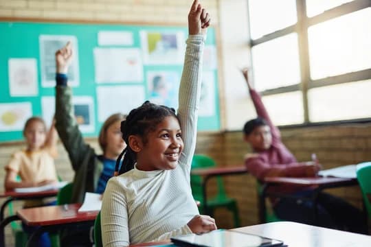Young children raising their hands in a classroom