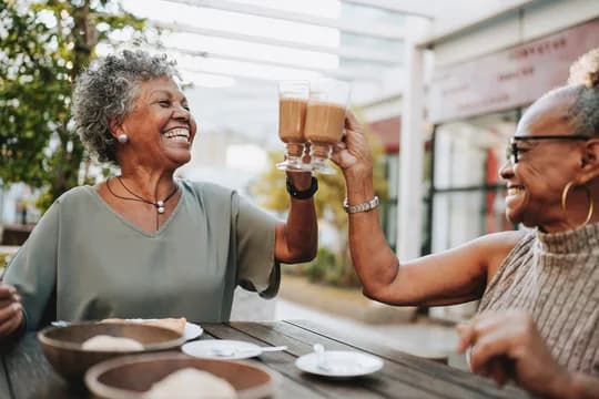 Two Older Women Sitting Outside Smiling Having Coffee